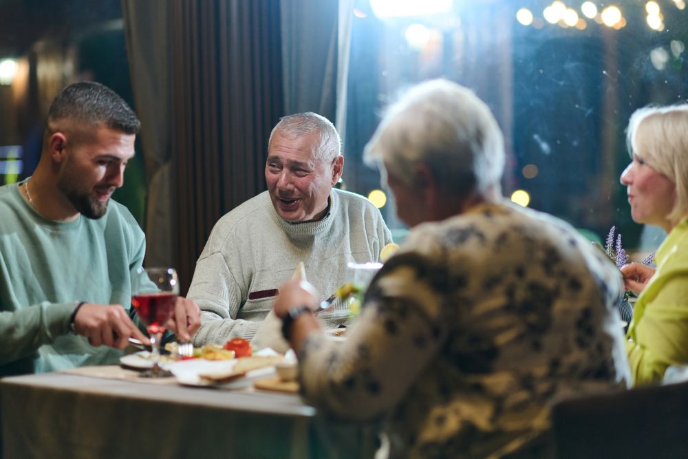 ersonnes âgées et jeunes adultes partageant un repas dans un restaurant bruyant, situation pouvant provoquer ou aggraver les acouphènes chez les seniors porteurs de troubles auditifs.