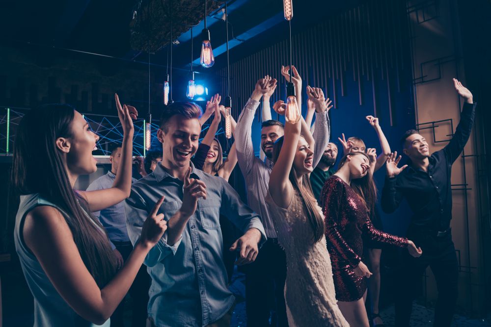  Jeunes adultes en train de faire la fête en discothèque avec musique forte et lumières vives, environnement à risque pour l’apparition d’acouphènes ou de sifflements d’oreille après exposition sonore prolongée.
